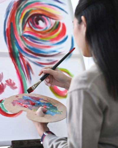 Rear view of female artist painting with watercolor on canvas.